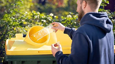 Mann wirft Kunststoffverpackung in Gelbe Tonne