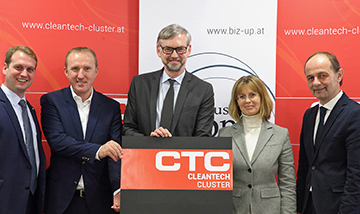 Fünf Personen stehend und in die Kamera schauend präsentieren das neuen Cleantech-Cluster-Logo (roter Hintergrund mit weißer Schrift)